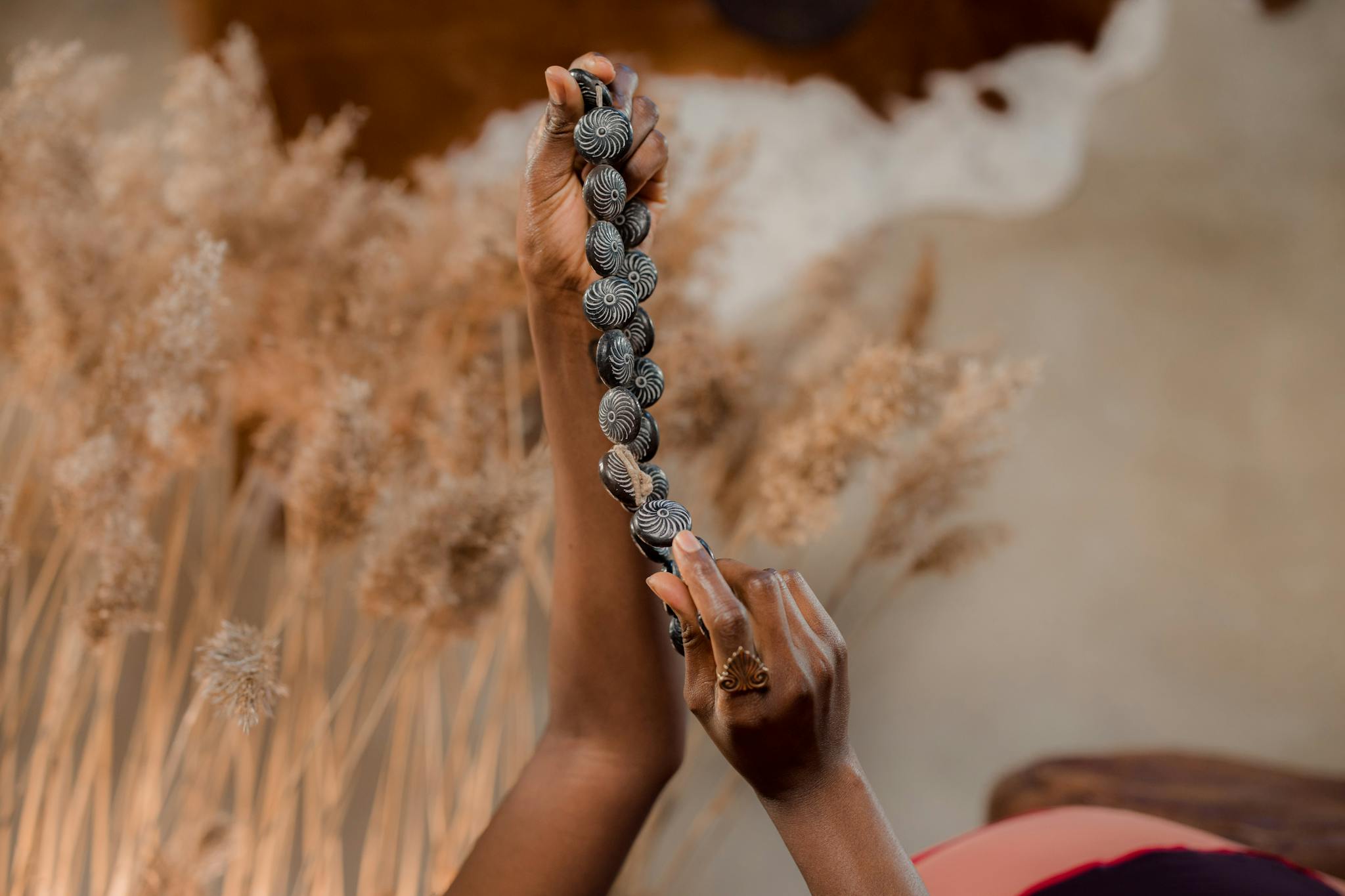 A close-up of hands holding a handcrafted beaded necklace against a soft background.