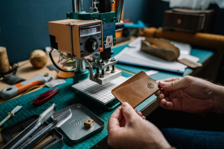 Close-up of a craftsman creating a handmade leather wallet using a hydraulic press in a cozy workshop.