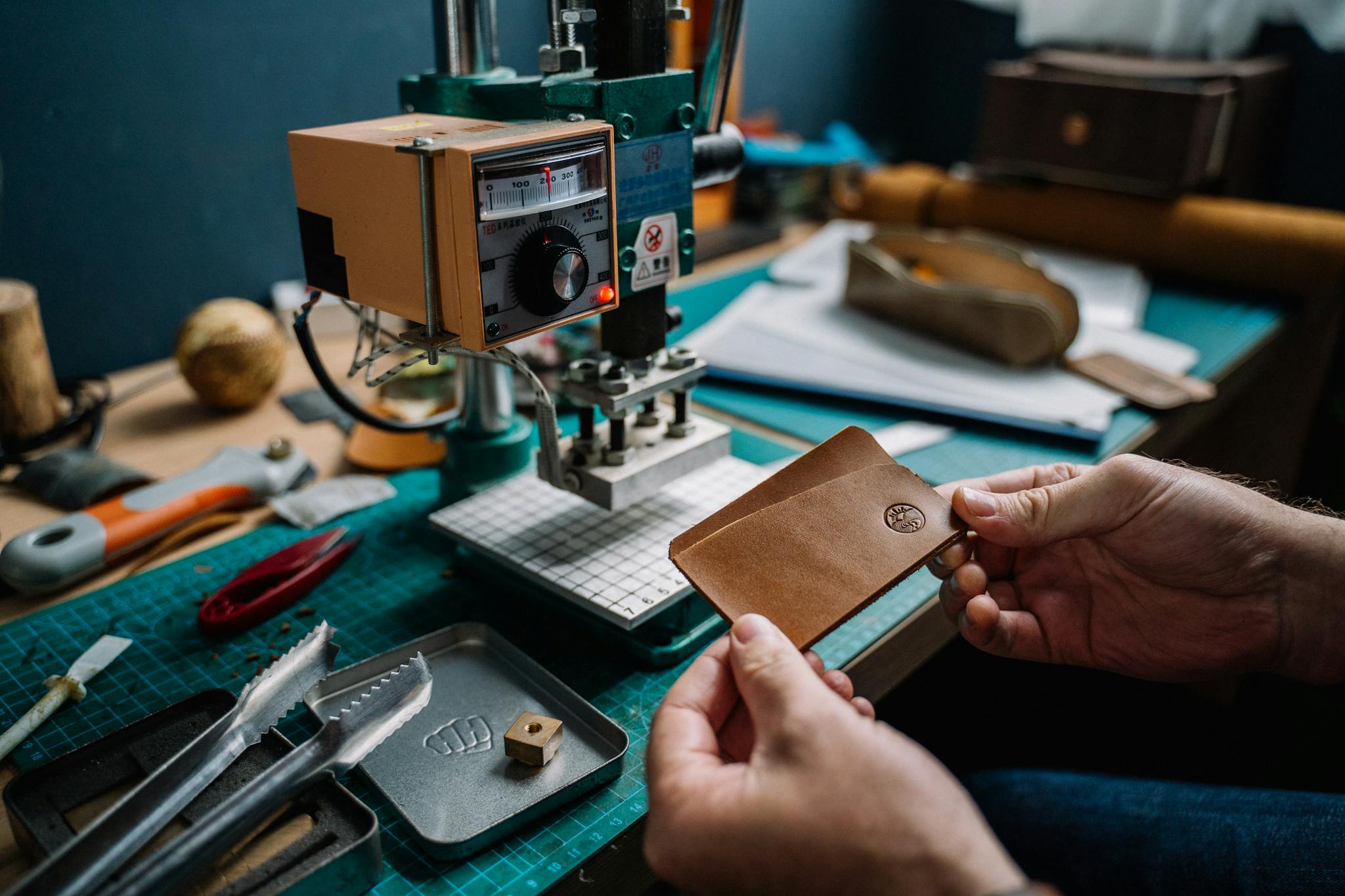 Close-up of a craftsman creating a handmade leather wallet using a hydraulic press in a cozy workshop.