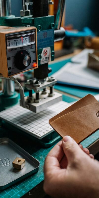 Close-up of a craftsman creating a handmade leather wallet using a hydraulic press in a cozy workshop.