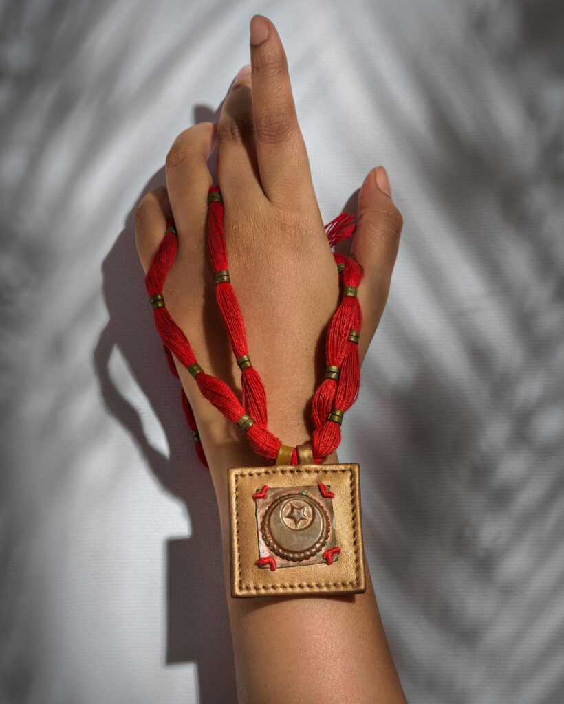 Close-up of a hand adorned with red and gold artisanal jewelry on a textured background.