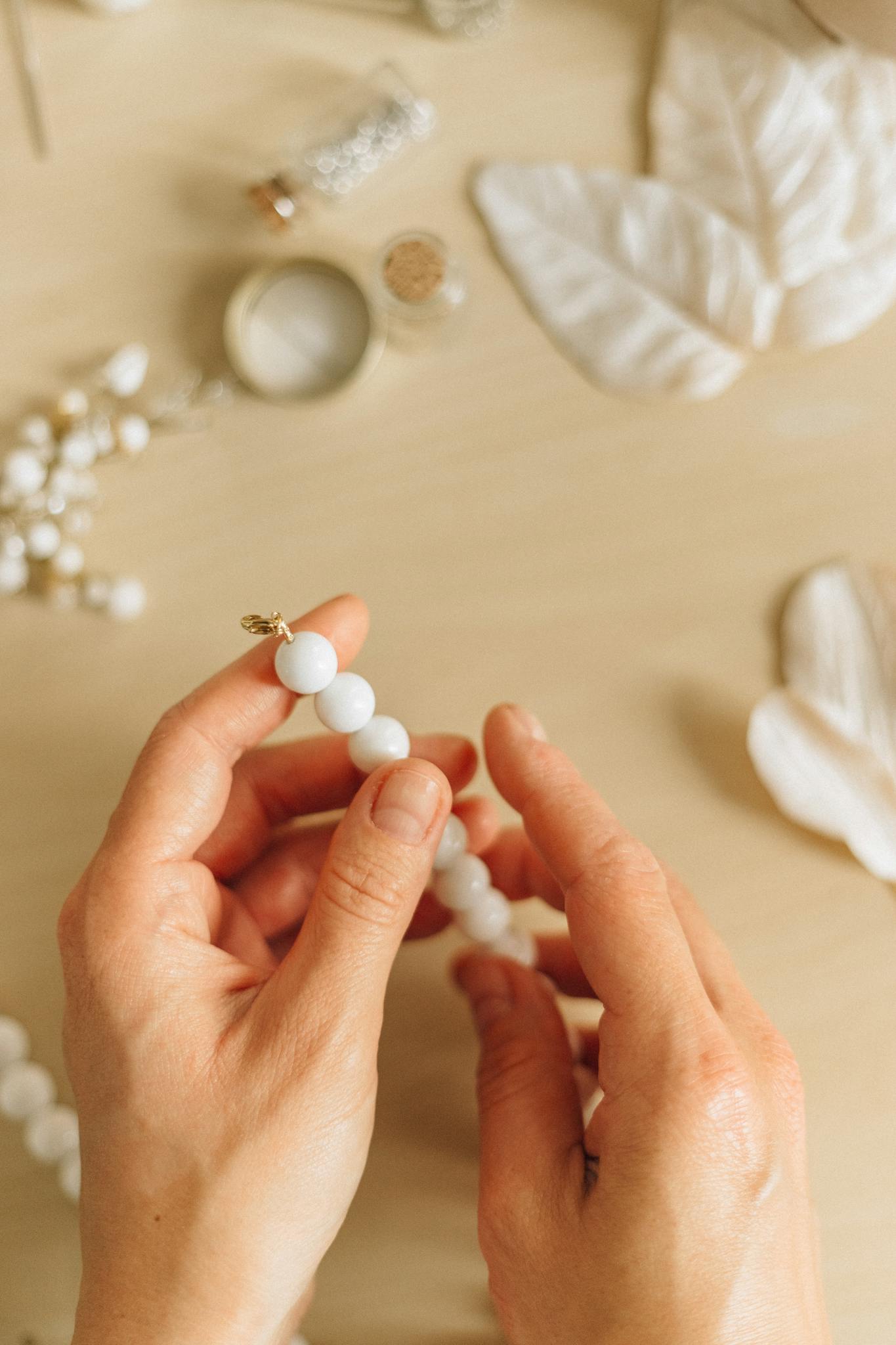 Close-up of hands crafting handmade bead necklace on a wooden surface.