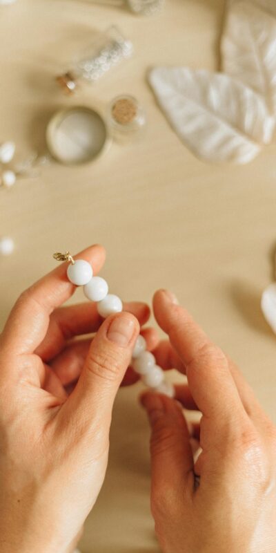 Close-up of hands crafting handmade bead necklace on a wooden surface.